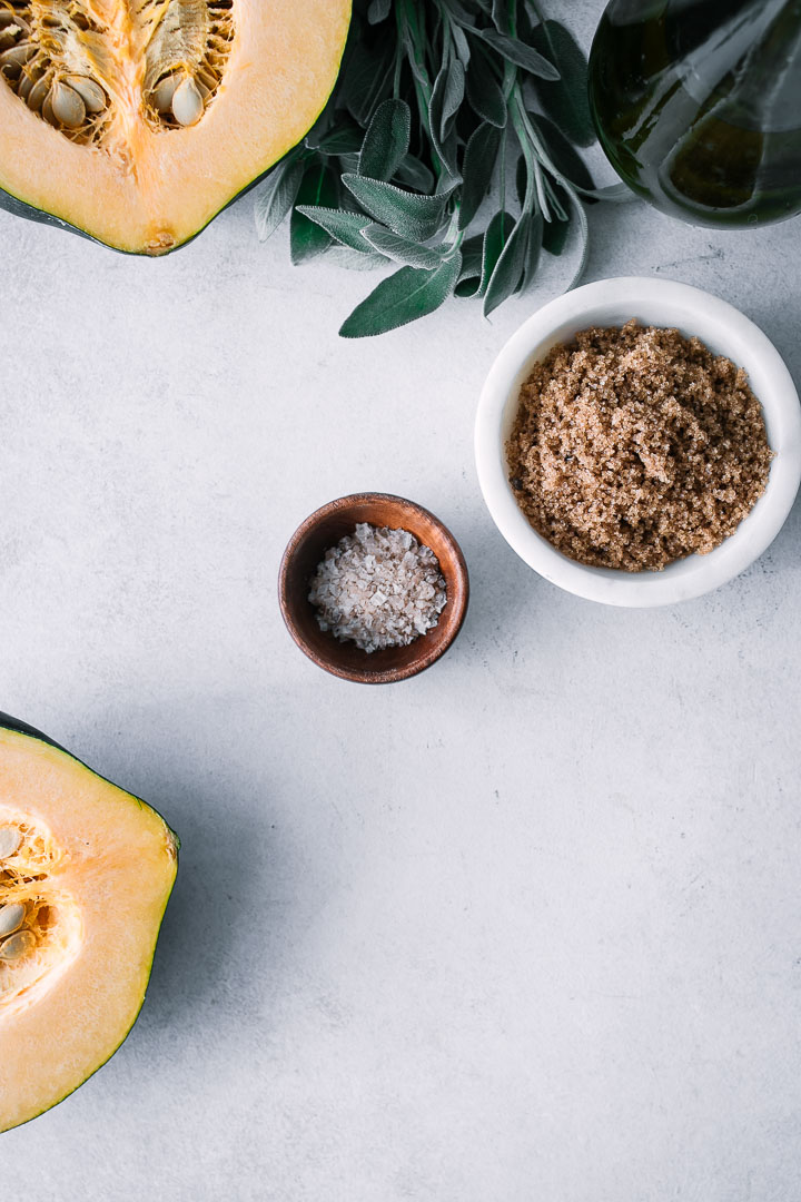 a white table with cut acorn squash, sage, brown sugar, and salt