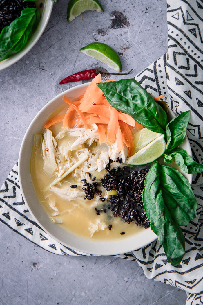 A thai-style soup with chicken and forbidden black rice with basil on a blue table.