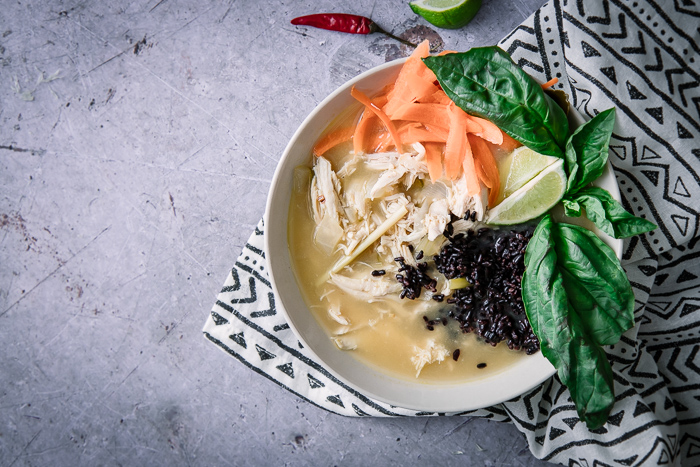 A thai-style soup with chicken and forbidden black rice with basil on a blue table.