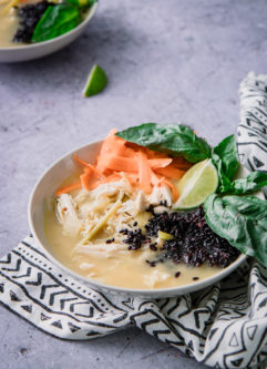 A thai-style soup with chicken and forbidden black rice with basil on a blue table.