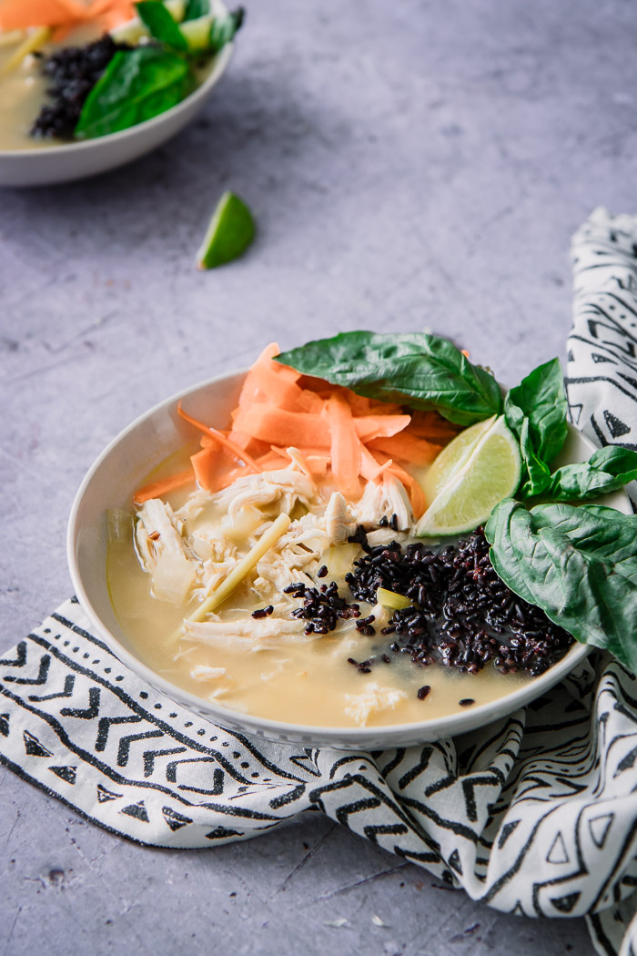 A thai-style soup with chicken and forbidden black rice with basil on a blue table.