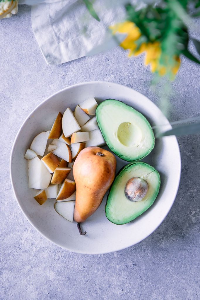 a white bowl with cut and whole pears and half an avocado
