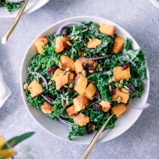 A green kale salad with orange squash with cranberries and pumpkin seeds