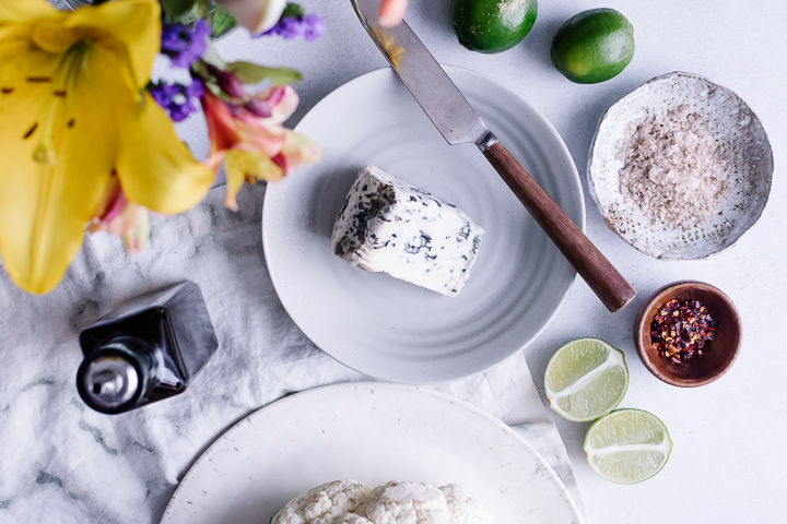 A piece of gorgonzola cheese with a cutting knife, cut limes, and yellow flowers.