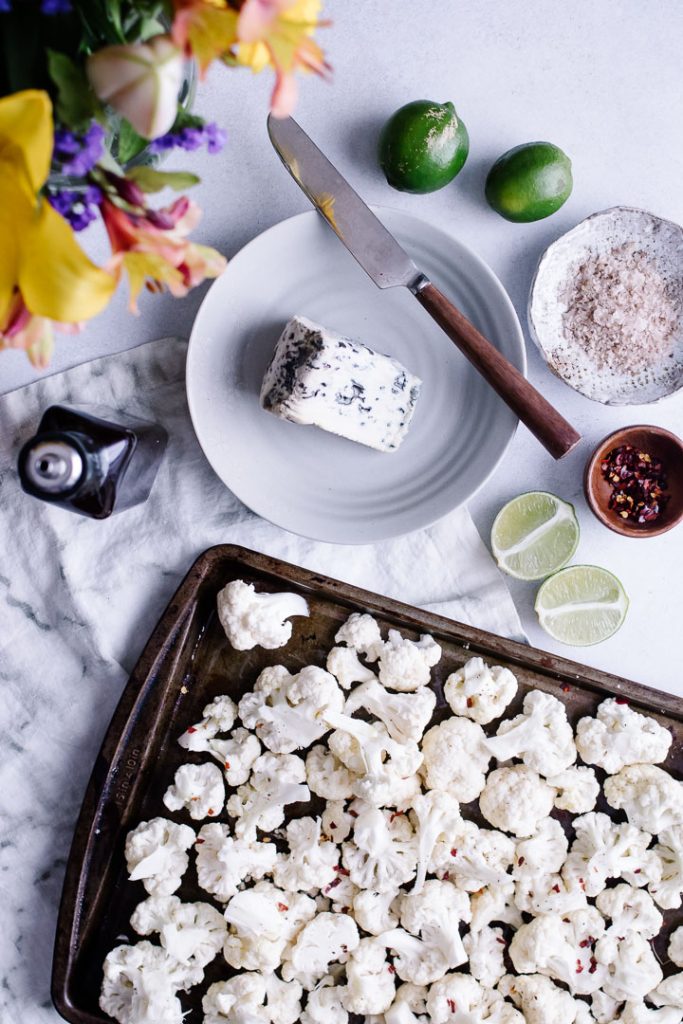 Cauliflower on a pan before roasting with a side of blue cheese, limes, and salt.