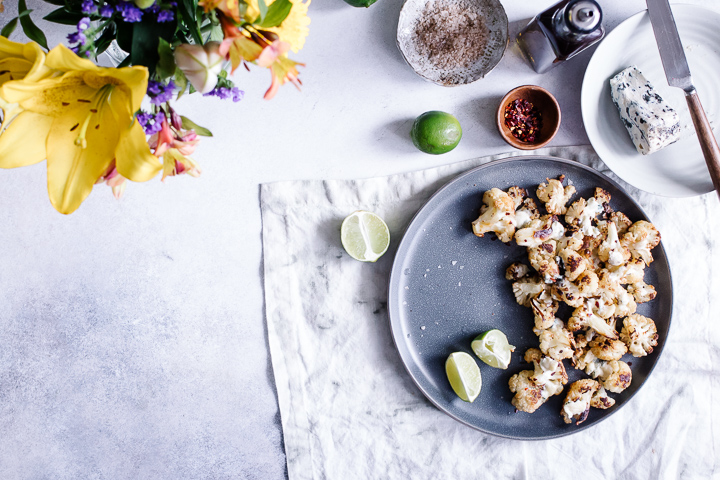 A set table with a blue plate with roasted cauliflower, a white napkin, and yellow flowers.