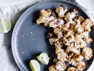 A pewter-colored plate with oven roasted cauliflower florets topped with cheese and lime juice.