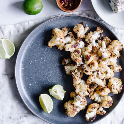 A blue plate with oven roasted cauliflower topped with gorgonzola and lime.