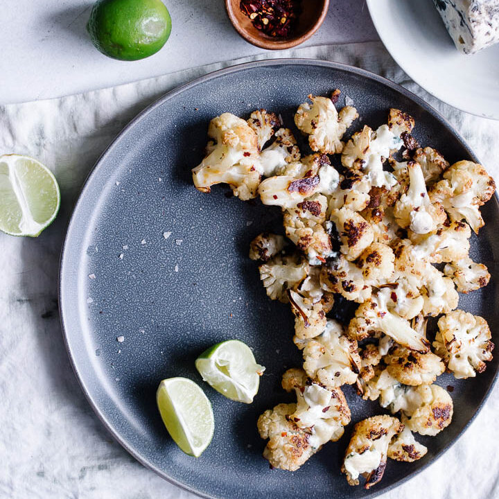 A blue plate with oven roasted cauliflower topped with gorgonzola and lime.
