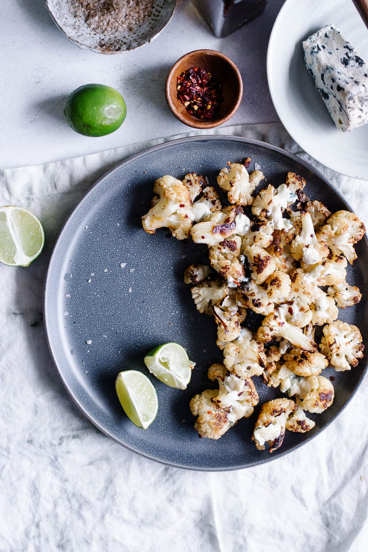 A blue plate with oven roasted cauliflower topped with gorgonzola and lime.