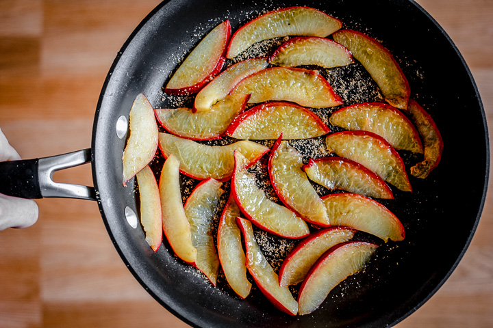 Sliced pluots cooking in a black pan.