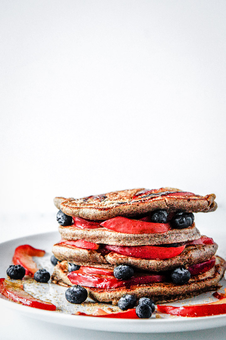 Pluot brown sugar buckwheat pancakes stacked on a white plate on a white table.