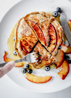 Pluot brown sugar buckwheat pancakes on a white plate being cut with a fork.