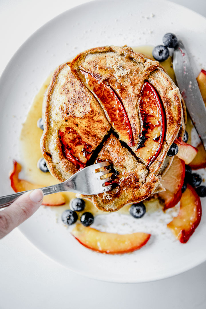 Pluot brown sugar buckwheat pancakes on a white plate being cut with a fork.