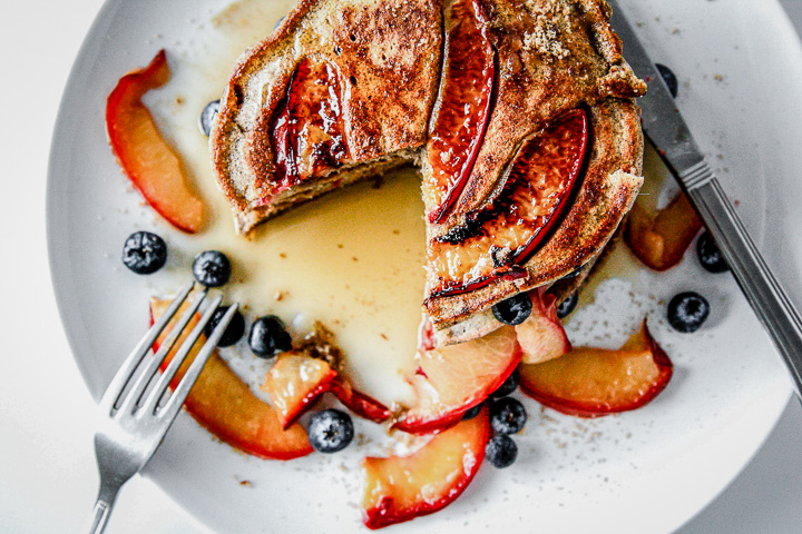 Pluot brown sugar buckwheat pancakes on a white plate being cut with a fork.