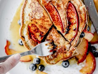 Pluot brown sugar buckwheat pancakes on a white plate being cut with a fork.