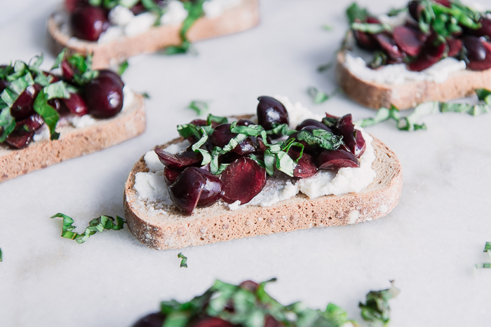 Toast with vanilla ricotta cheese with cherries and basil on top of a white marble table.