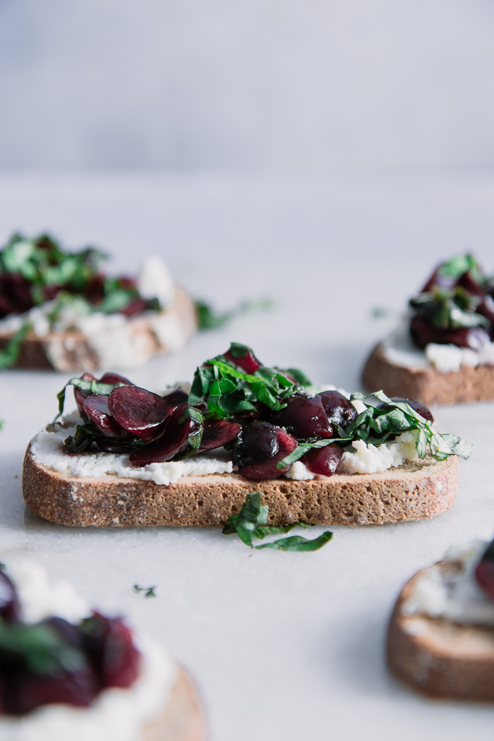 Toast with vanilla ricotta cheese with cherries and basil on top of a white marble table.