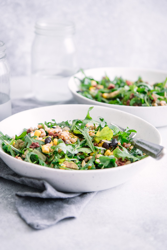 A farro and arugula salad in two bowls on a white table.