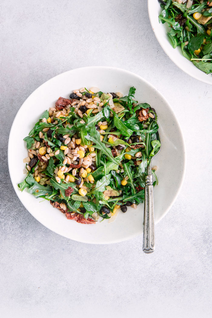 A grain and greens salad in a while bowl on a blue table with a silver fork.