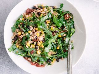 A green and grains salad with two white bowls with the words "black bean corn farro salad" in black and red writing.