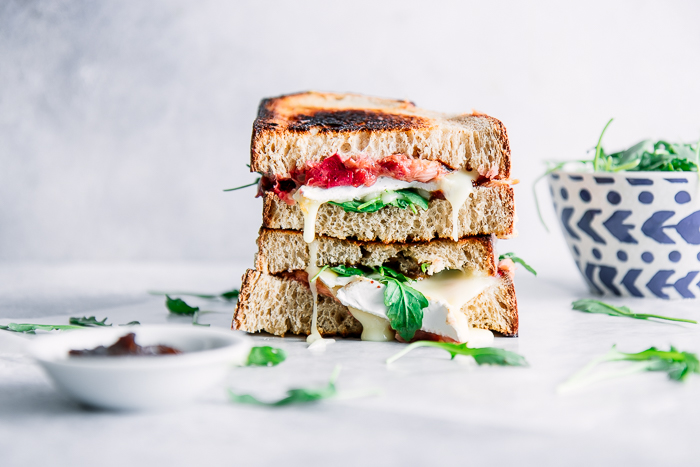 A stacked sandwich with brie and rhubarb on a white table and gooey cheese.