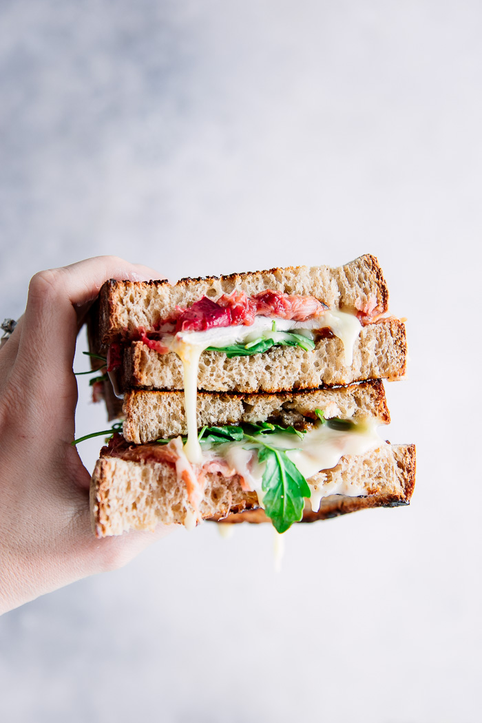 A hand holding a cut brie and rhubarb sandwich with oozing cheese.