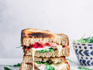 A cut sandwich stacked on top of one another with melted brie cheese, arugula, and whole grain bread and the words "roasted rhubarb brie sandwich" in black letters.