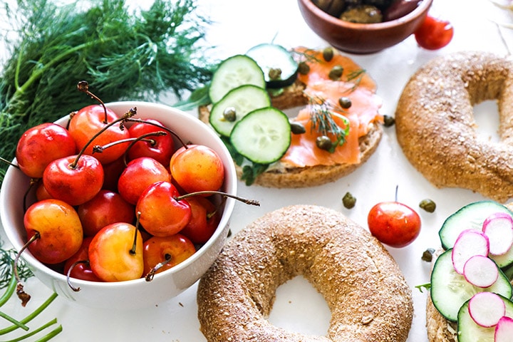 cut bagels on a white table with smoked salmon lox, cucumbers, and fresh dill