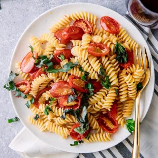 A white plate with Italian cold pasta salad with fusilli pasta, tomatoes, and basil with a gold fork.