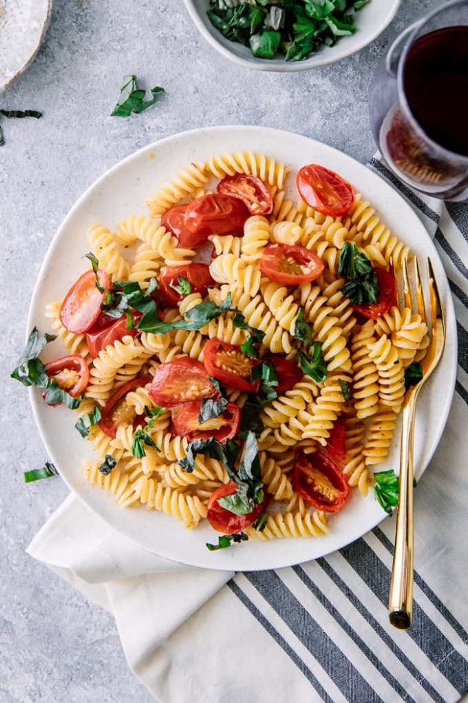 A white plate with Italian cold pasta salad with fusilli pasta, tomatoes, and basil with a gold fork.