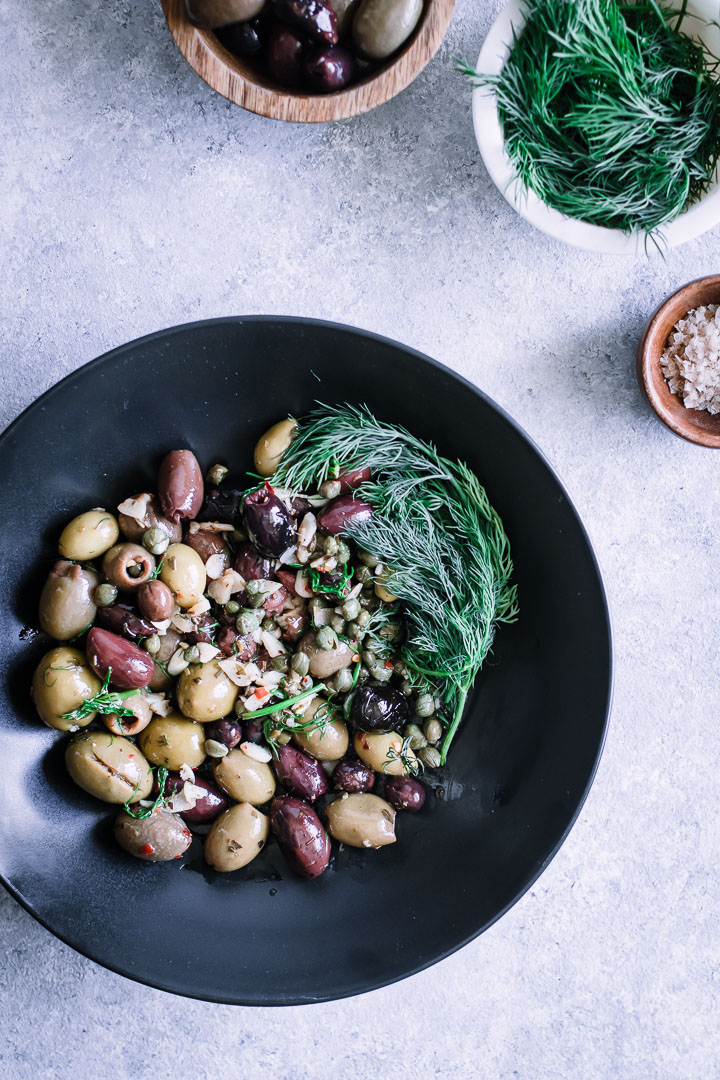 A picture of a table from above with a bowl of marinated olives and a bowl of salt.