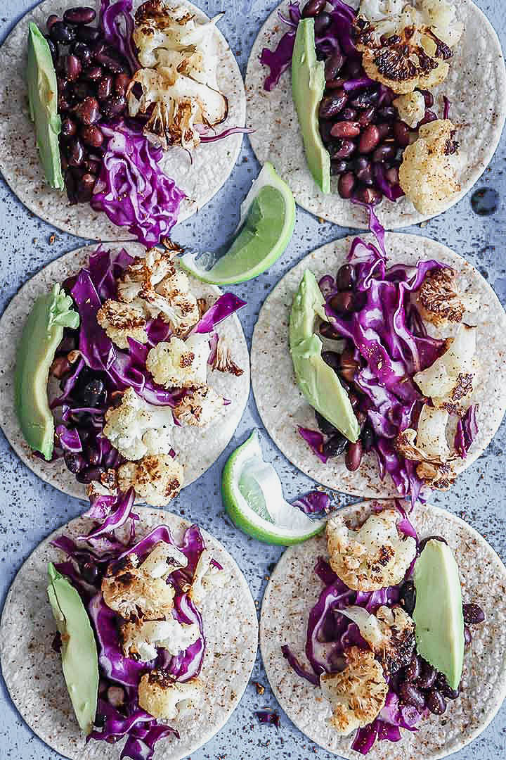 Six chili lime cauliflower tacos on a blue table.