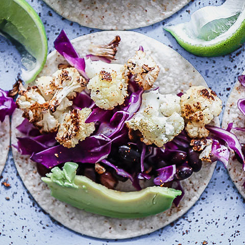 A vegan taco with cauliflower, chili, cabbage, and lime on a blue table.