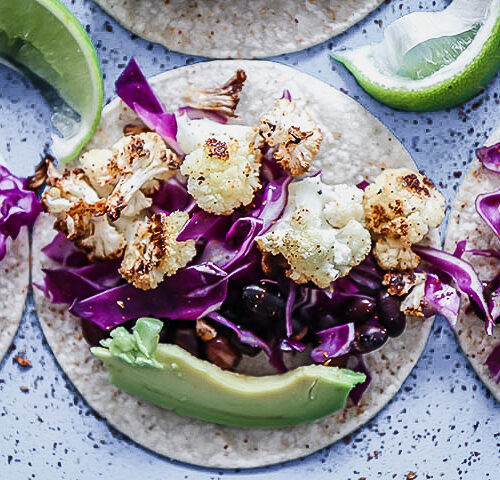 A vegan taco with cauliflower, chili, cabbage, and lime on a blue table.
