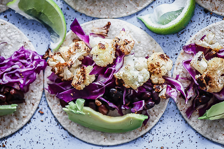 A vegan taco with cauliflower, chili, cabbage, and lime on a blue table.