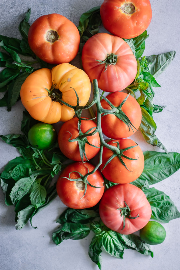 An arrangement of fresh tomatoes with basil on a white table.