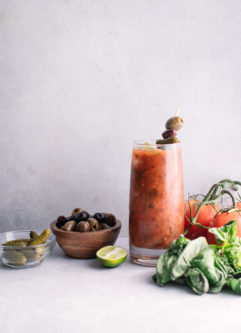A tall glass of homemade spicy bloody mary mix with pickles, olives, and herbs.