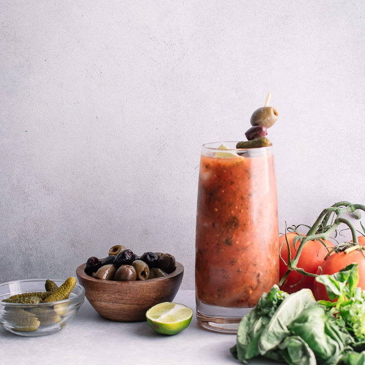A tall glass of homemade spicy bloody mary mix with pickles, olives, and herbs.