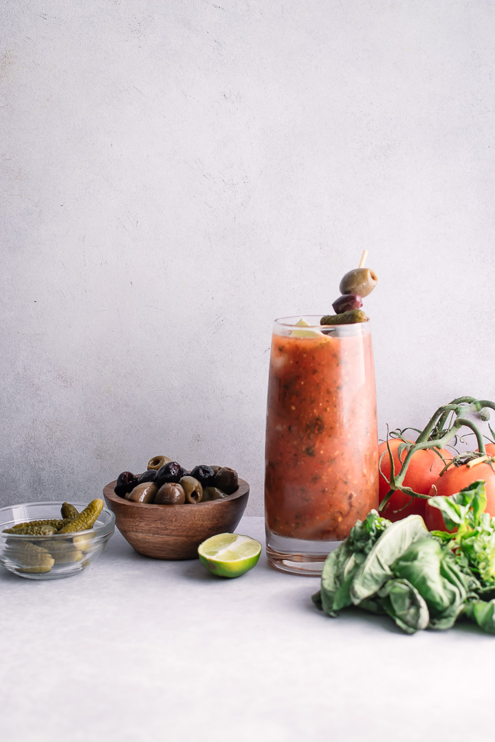 A tall glass of homemade spicy bloody mary mix with pickles, olives, and herbs.