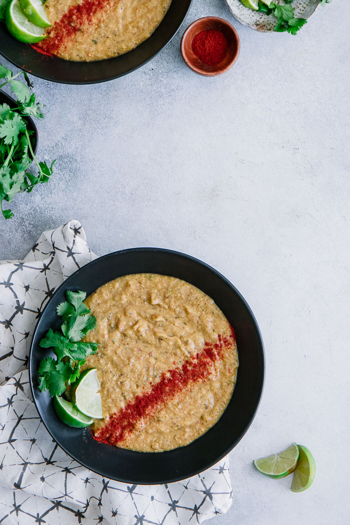 A black bowl of vegan corn and potato soup on a white table with cilantro and lime.