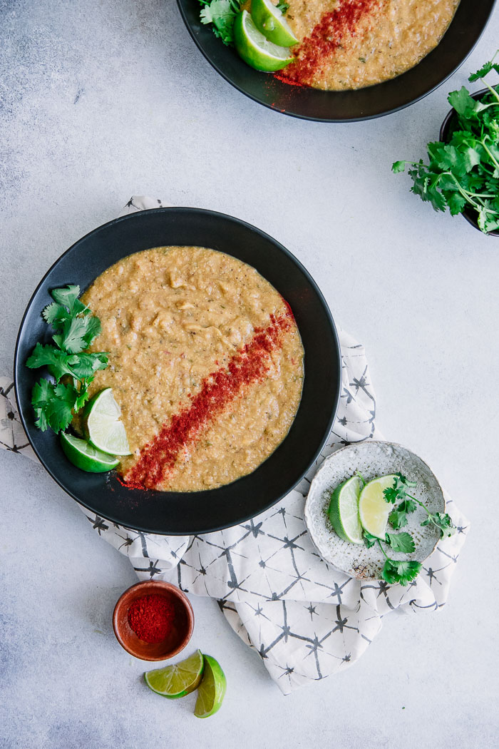 A bowl of vegan corn and potato chowder with paprika, cilantro, and lime garnish on a white table.