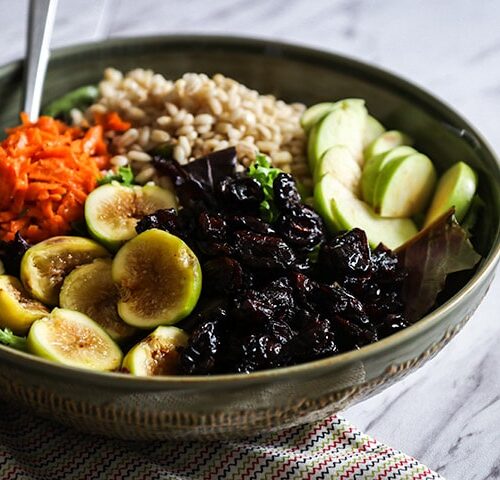 a bowl of warm grains and fall produce on a white table