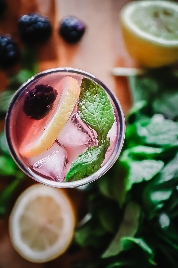 A glass of boozy blackberry lemonade on a cutting board with fresh fruit.