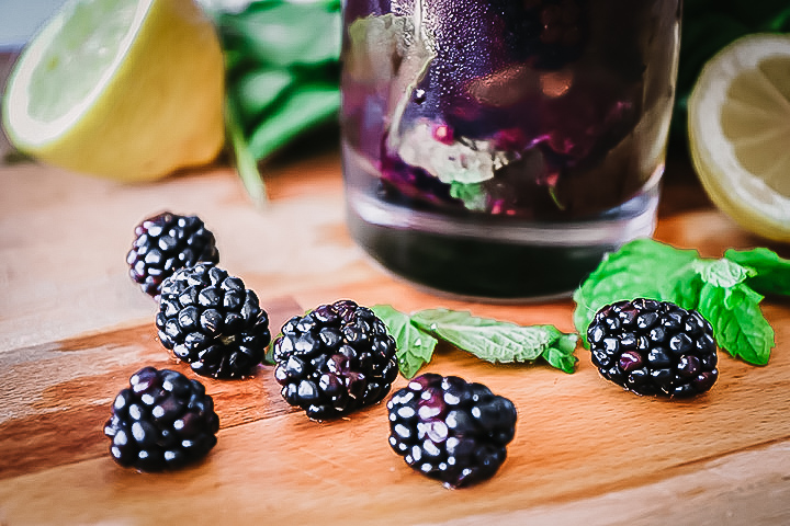A glass of boozy blackberry lemonade on a cutting board with fresh fruit.