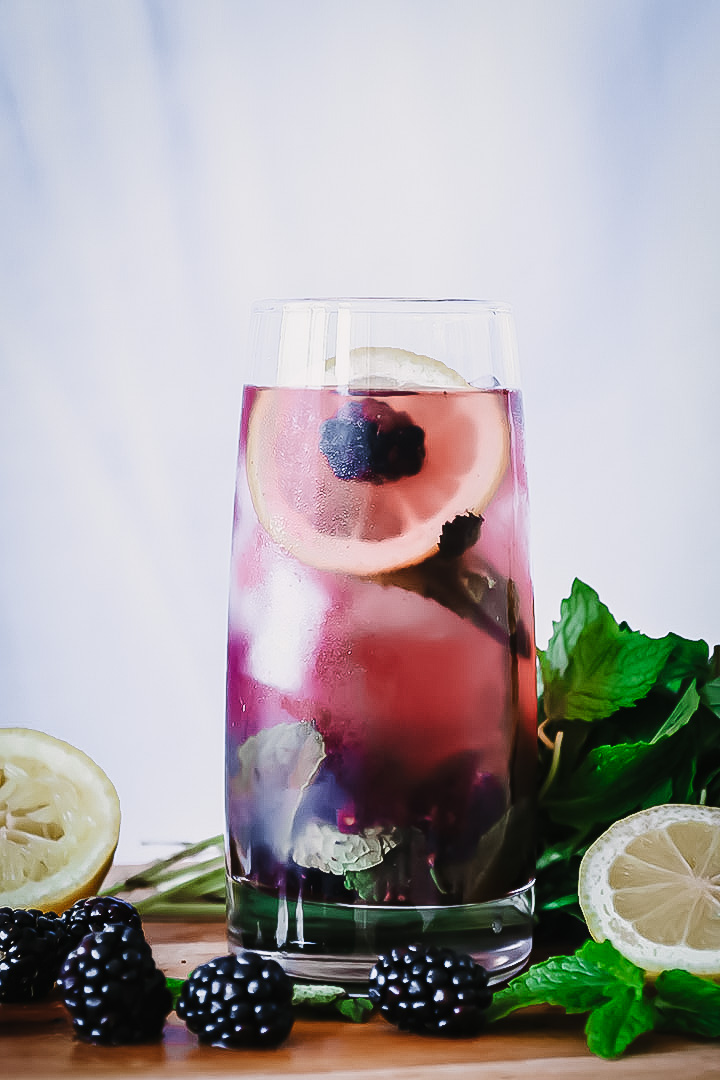 A glass of boozy blackberry lemonade on a cutting board with fresh fruit.