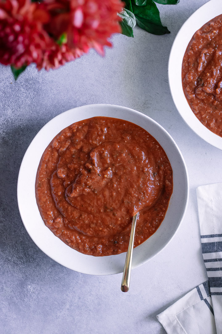 Two bowls of tomato soup with fresh flowers on a blue table.