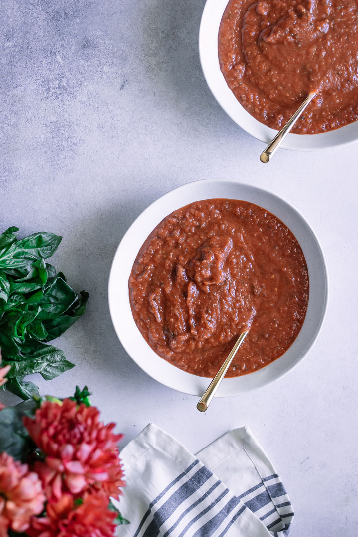 A white bowl with tomato soup on a blue table.