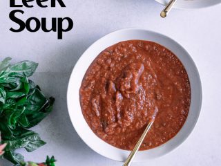 A bowl of red tomato soup with the words "roasted tomato leek soup" in black writing.