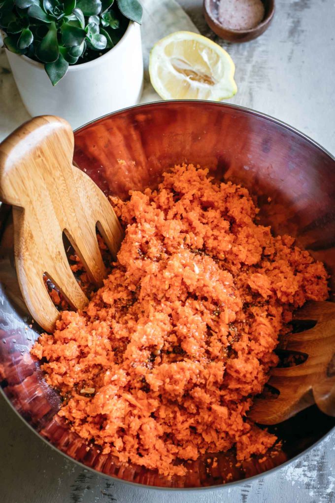 shredded carrots and dressing in a large mixing bowl with a wooden spoon